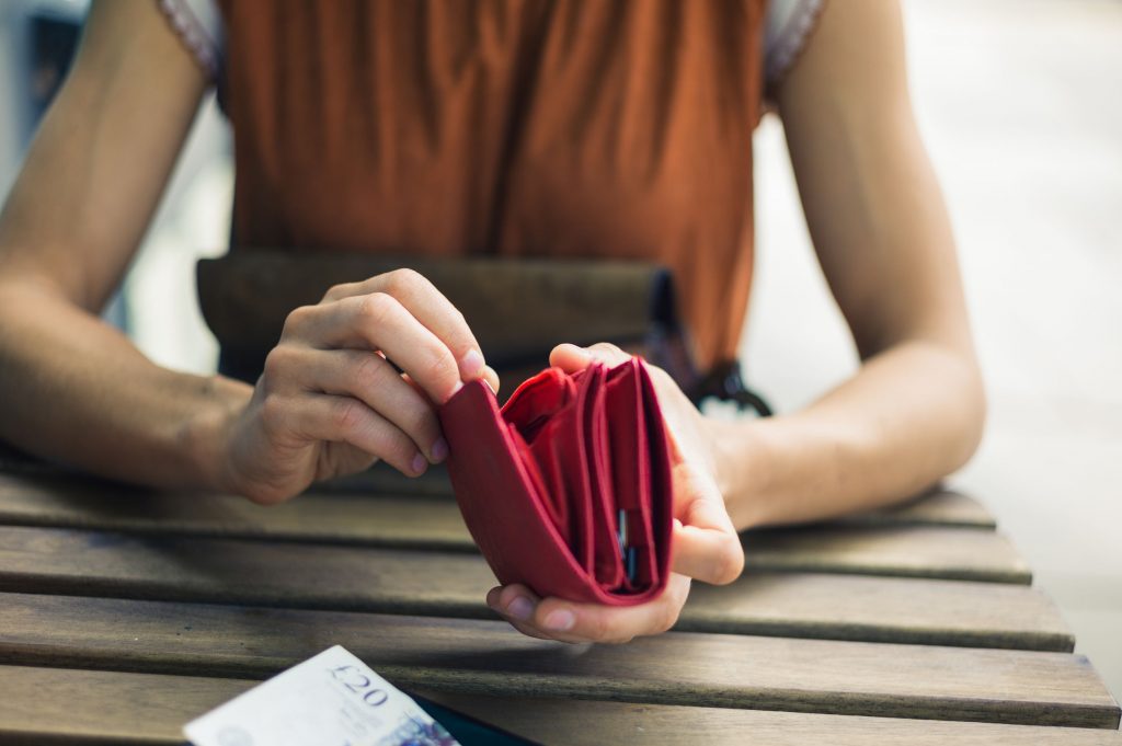 42882867 - a young woman is sitting outside and is opening her purse to get some cash for paying her bill at a cafe