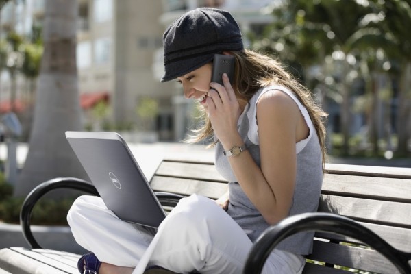 Young woman, talking on a mobile phone and using a laptop