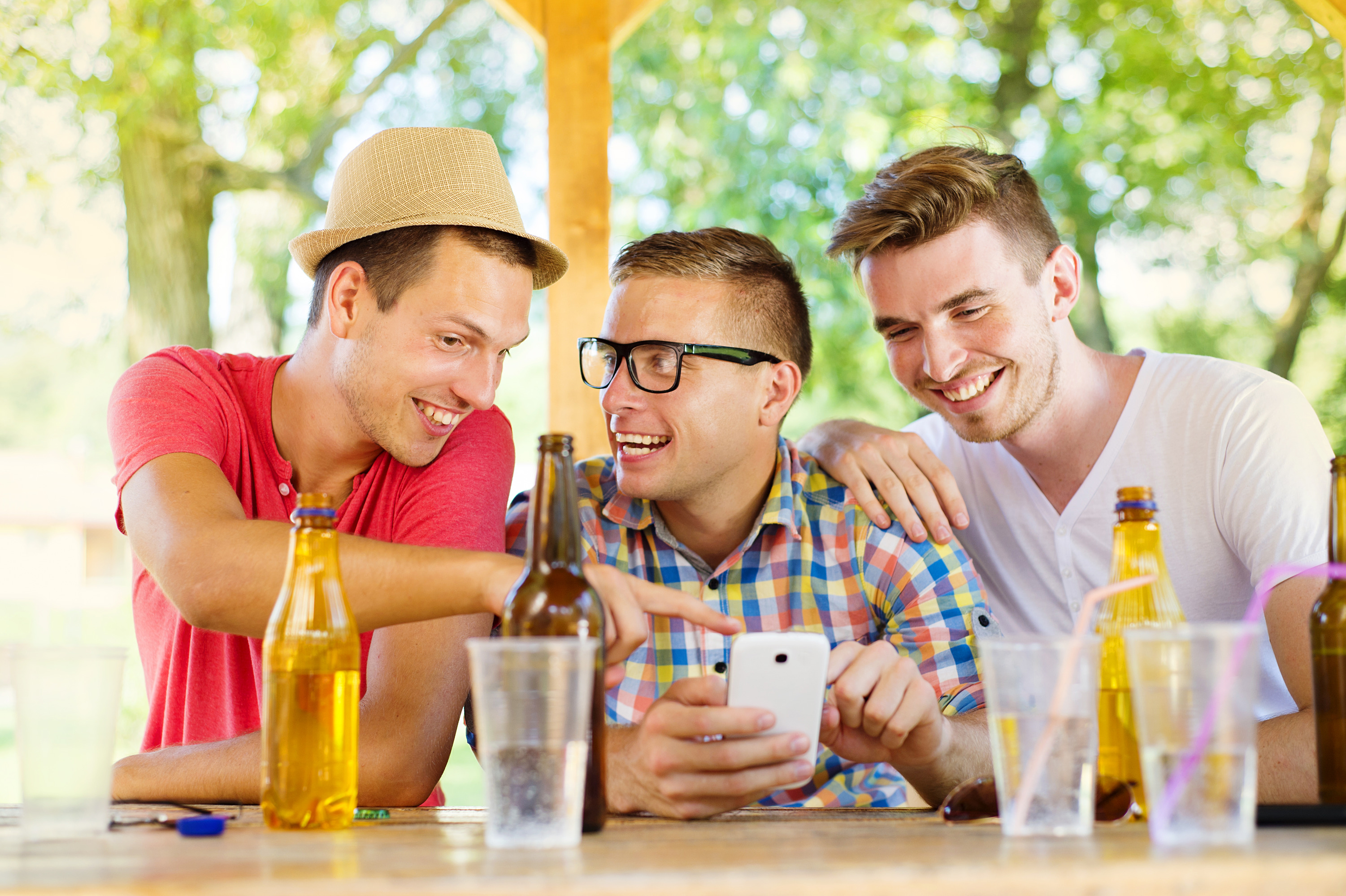 Three happy friends drinking and having fun with smartphone in pub garden